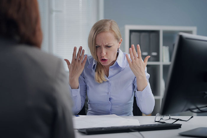 Woman upset and frustrated during a tense office meeting about a man reported to HR for inappropriate behavior.