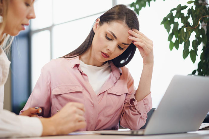 Young woman reflecting on her cancer surgery story while discussing with coworker in a bright office setting.