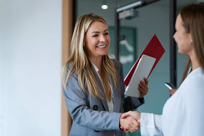 Young woman sharing cancer surgery story while shaking hands with coworker in a professional office setting.