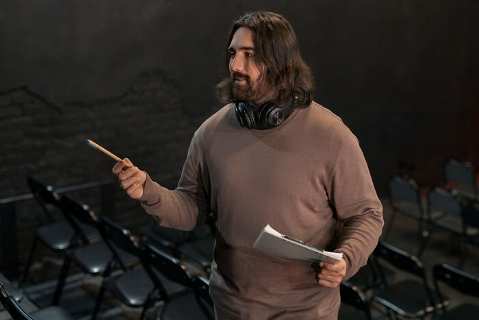 Man with headphones holding pencil and clipboard in empty classroom, illustrating high school secrets discovered later