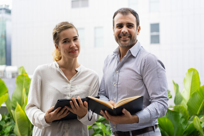 Two people smiling outdoors holding a tablet and notebook, discussing high school secrets.