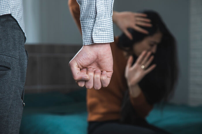 Man's clenched fist near woman shielding face on bed, illustrating high school secrets.