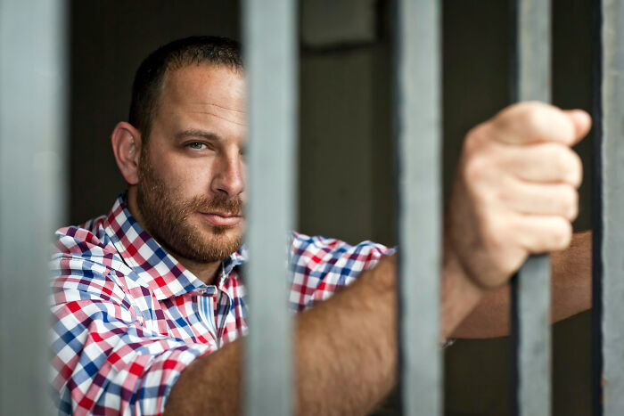 Man behind bars in plaid shirt, contemplative, symbolizing high school secrets revealed after graduation