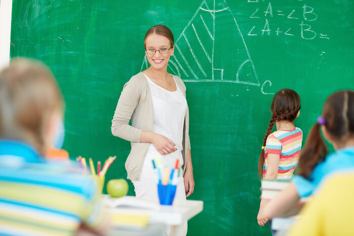 Teacher instructing students at chalkboard with geometry diagram, classroom scene illustrating high school secrets discovery