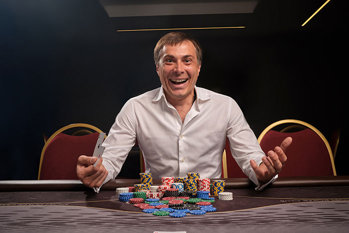 Man at poker table smiling confidently with poker chips, showing intelligence so sharp it almost feels scary.