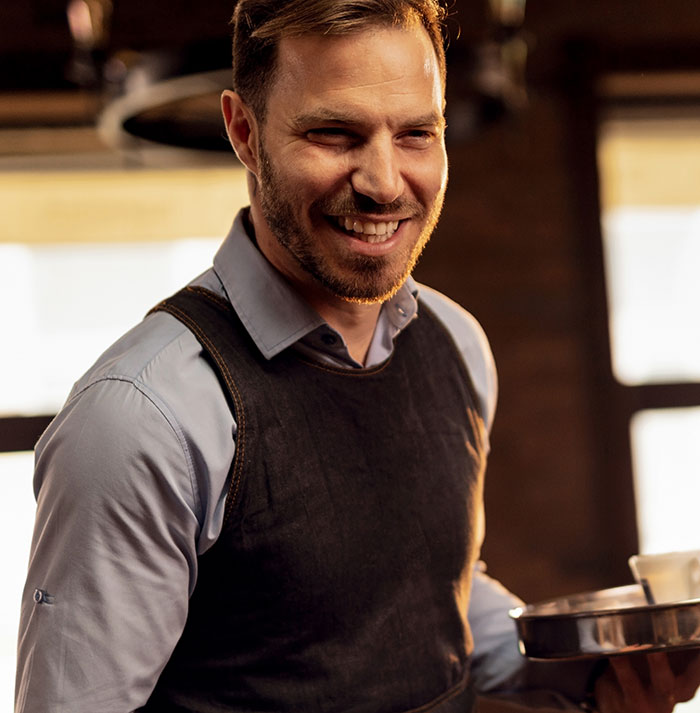 Man with a sharp intelligence smiling confidently while holding a tray in a warm, softly lit setting
