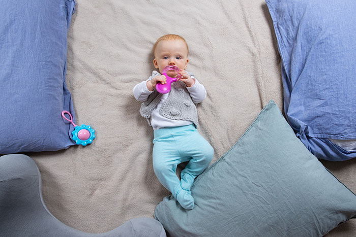Baby lying on bed surrounded by pillows and toys, capturing a moment of sharp intelligence and curiosity.