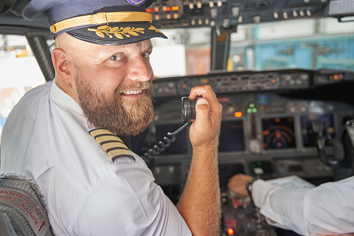 Pilot with a sharp intelligence speaking into a radio headset inside a commercial airplane cockpit.