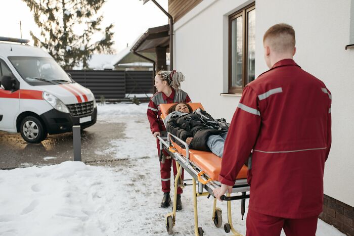 Two paramedics in red uniforms wheeling a woman on a stretcher outside near an ambulance, illustrating creepy facts about the human body.