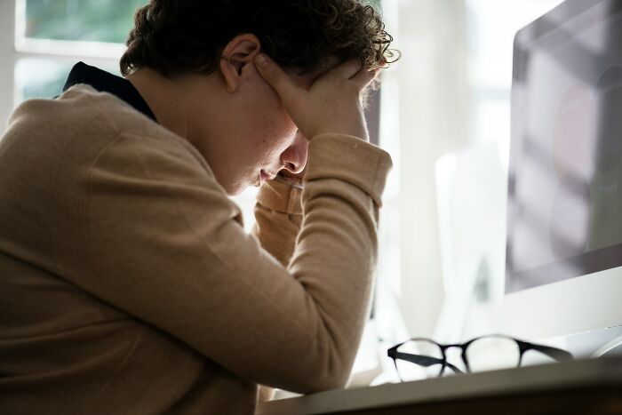 Person stressed at desk holding head, illustrating the impact of worst coworkers on work experience.