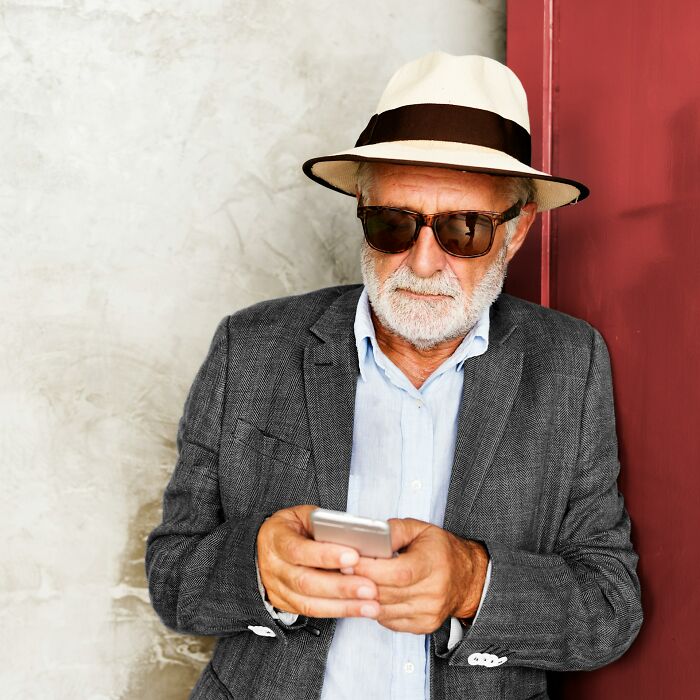 Older man in sunglasses and hat looking at phone, representing DNA test results and unexpected discoveries.