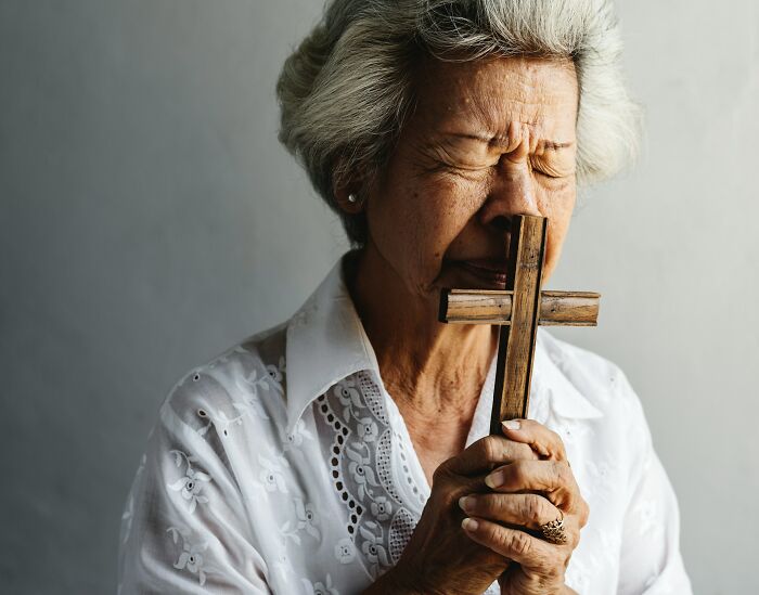 Elderly woman holding a wooden cross with eyes closed, reflecting emotions linked to DNA test plot twists.
