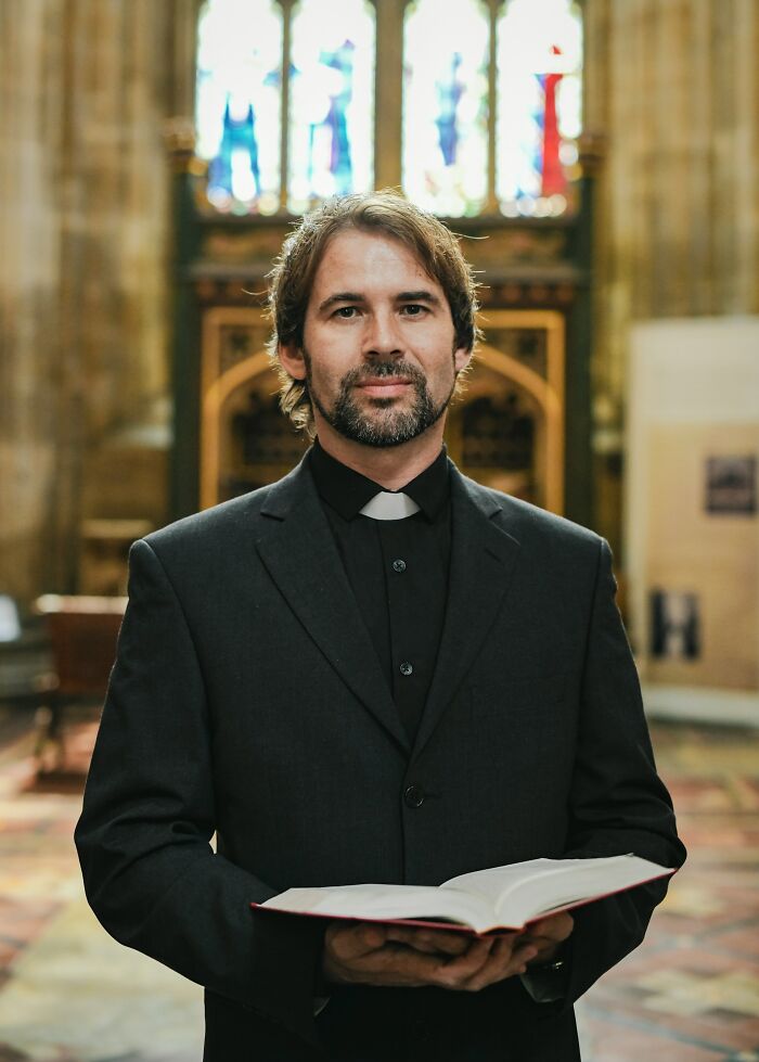 Man in clerical collar holding a book inside a church, representing former cult members revealing their experiences.