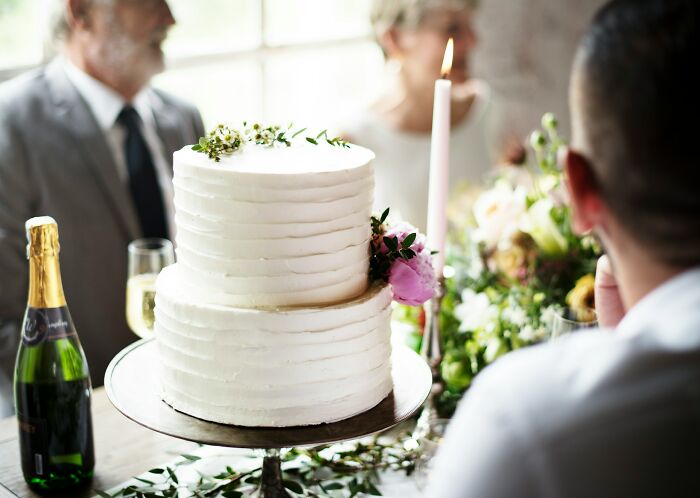 Two-tier white wedding cake with flowers and champagne on table during candid wedding moments celebration.