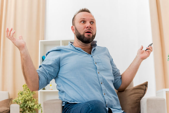 Man in a blue shirt gesturing with hands sitting on chair, expressing surprise, no dad brother cooking food visible.