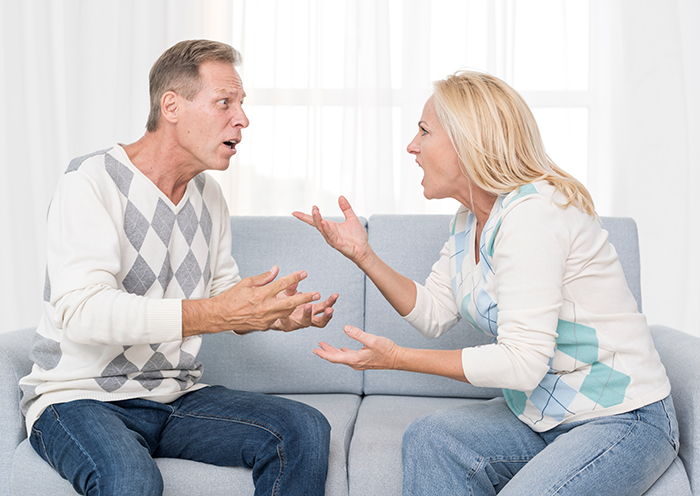 A middle-aged couple arguing on a couch as mom reacts devastated by proof of dad&rsquo;s months-long affair.