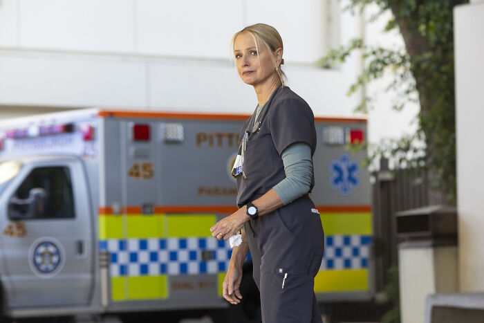 Katherine LaNasa as Nurse Dana in dark scrubs standing near an ambulance in a hospital setting. - 1