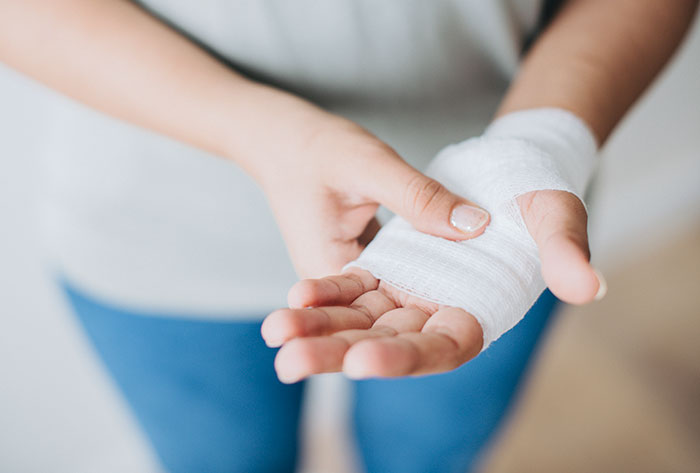 Woman wrapping her injured wrist with a bandage after using a dangerous gift despite husband's warning.