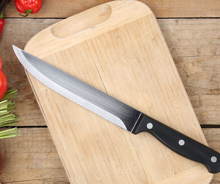 Sharp kitchen knife with black handle on wooden cutting board, symbolizing dangerous gift warning from husband to wife.