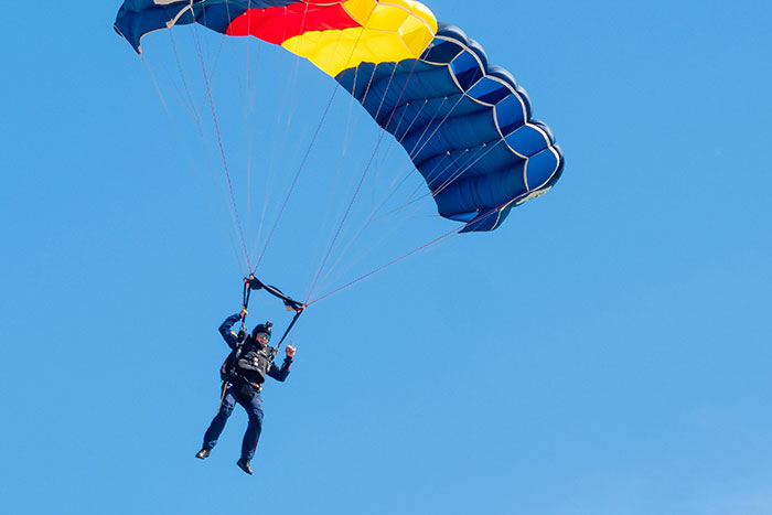 Person skydiving with a colorful parachute against a clear blue sky, illustrating dangerous things people did.