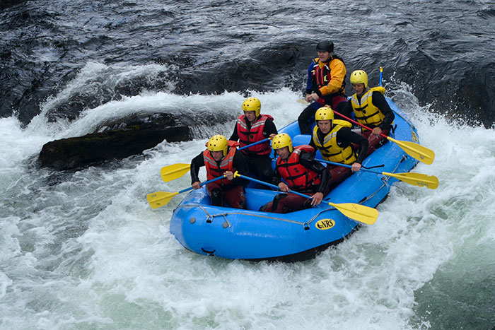 Group of people wearing helmets and life jackets rafting through dangerous whitewater rapids, showcasing risky activities.