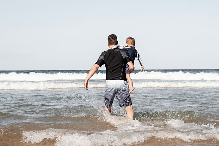 Man carrying child into ocean waves, illustrating one of the most dangerous things people willingly or unwillingly did.