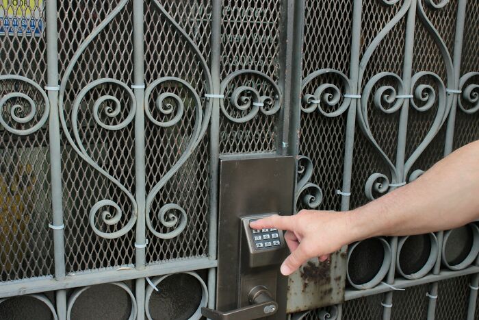 Person pressing keypad on secure metal gate lock, illustrating safety measures women use while living alone.