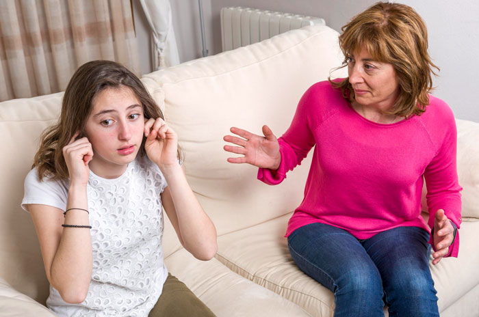Annoyed mom and 15-year-old daughter arguing on couch as daughter refuses to do chores seen as pick me behavior.