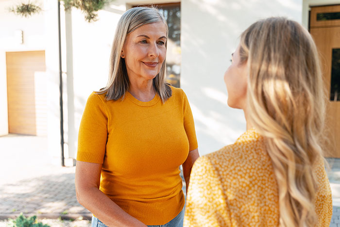 Middle-aged mom in orange top talking to daughter outdoors about DNA test concerns and family matters. Middle-aged mom in orange top talking to daughter outdoors about DNA test concerns and family matters.