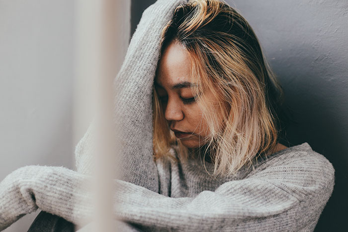 Young woman with blonde hair in a gray sweater looks contemplative, reflecting on DNA test conflict with her mom. Young woman with blonde hair in a gray sweater looks contemplative, reflecting on DNA test conflict with her mom.