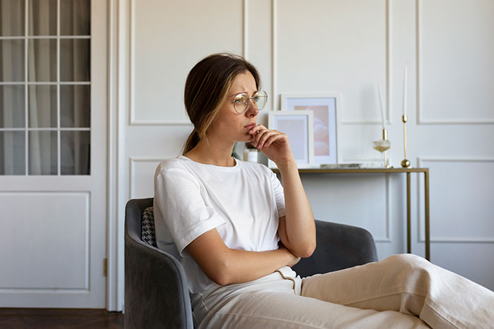 Young woman thoughtfully sitting in chair, symbolizing mom against daughter getting a DNA test, reflecting family conflict and curiosity. Young woman thoughtfully sitting in chair, symbolizing mom against daughter getting a DNA test, reflecting family conflict and curiosity.