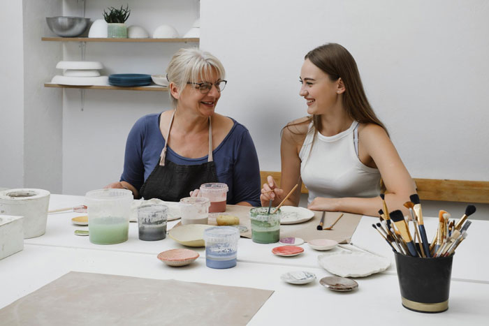 Mom and daughter painting tiny cottages together at a table, highlighting mom’s mixed feelings about daughter's hobby. Mom and daughter painting tiny cottages together at a table, highlighting mom’s mixed feelings about daughter's hobby.