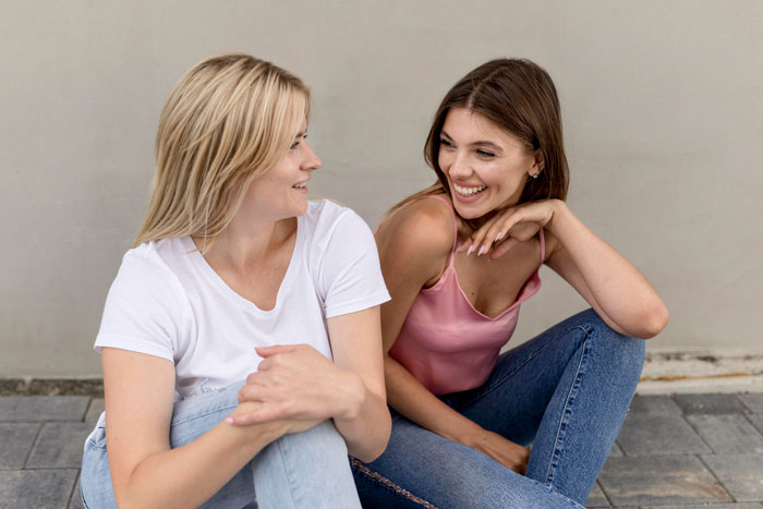 Two women sitting and smiling, illustrating a mom wishing her daughter were a cheerleader instead of building tiny cottages. Two women sitting and smiling, illustrating a mom wishing her daughter were a cheerleader instead of building tiny cottages.