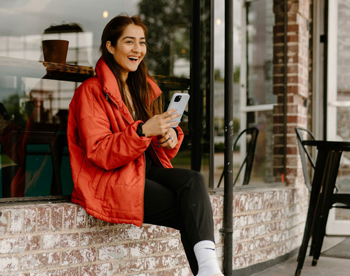 Teen girl in red jacket smiling and holding a phone, showing stepsister&rsquo;s support against stepmom&rsquo;s criticism about spending.