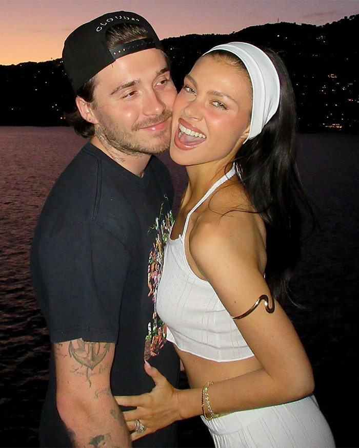 Young couple smiling and hugging at sunset by the water, relating to David Beckham public teasing son family rift crisis.