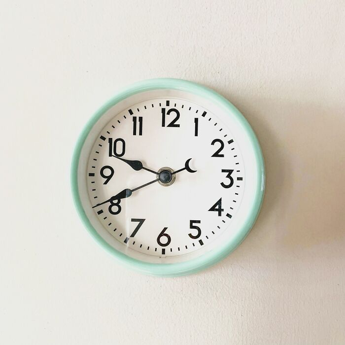 Round wall clock with green rim showing 9:40 against a plain white wall, symbolizing shipping containers timing and solutions.