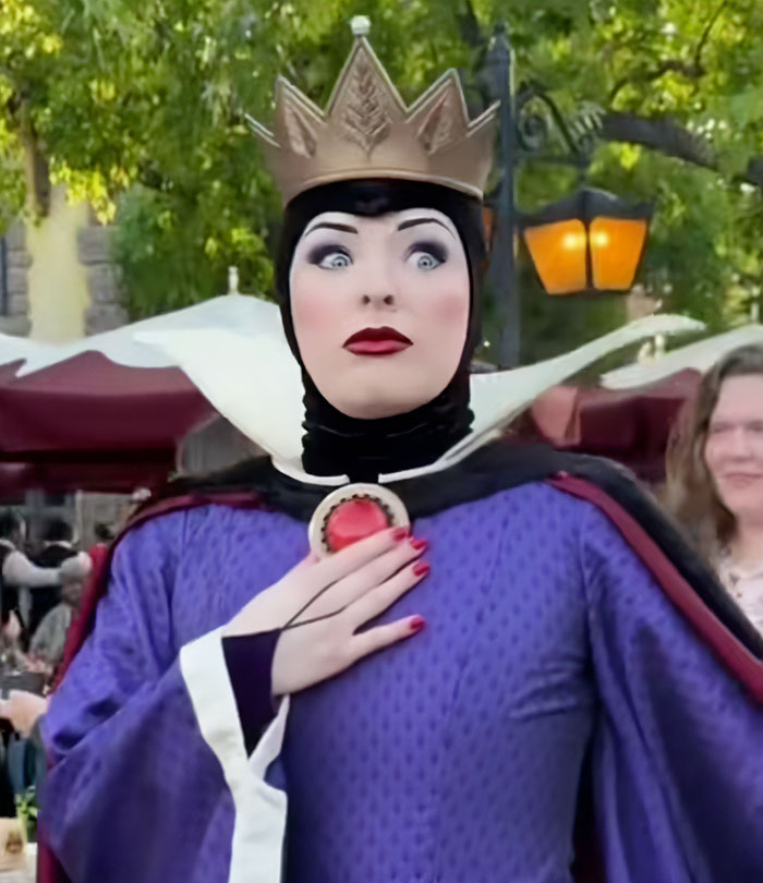 Evil Queen character in purple costume and crown, reacting with surprise while posing at an outdoor Disney park setting.