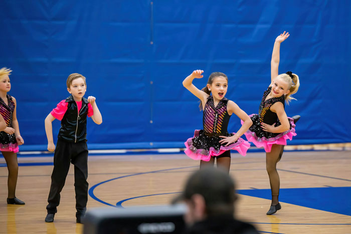 Children performing a dance routine in a gymnasium, illustrating themes of trust and deception like a husband telling wife about camping trip.