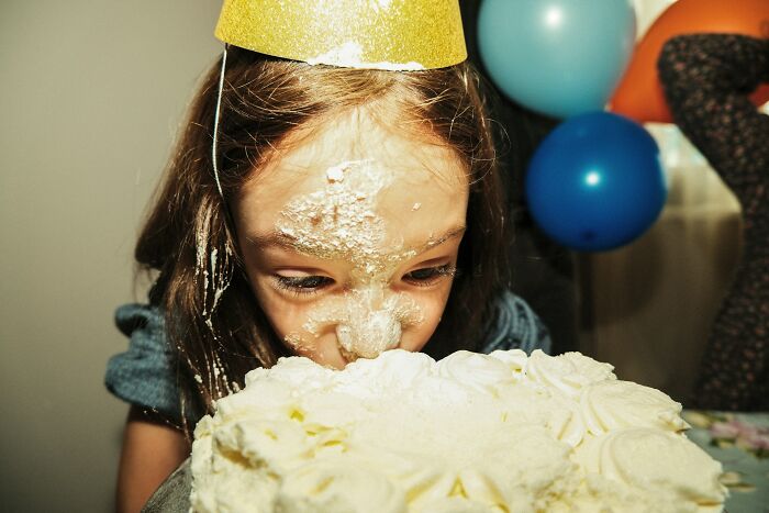 Young girl with a party hat smashing her face into a birthday cake, illustrating cultural differences shared by 35 people worldwide.