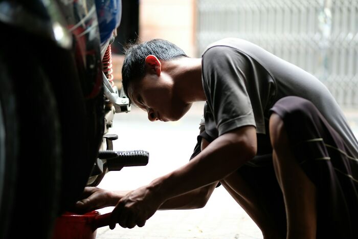 Person demonstrating surprising intelligence while repairing a motorcycle in a dimly lit garage setting.