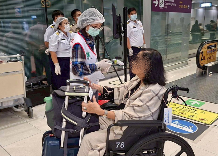 Healthcare worker wearing protective gear assisting a passenger in wheelchair amid incurable virus outbreak and airport restrictions.