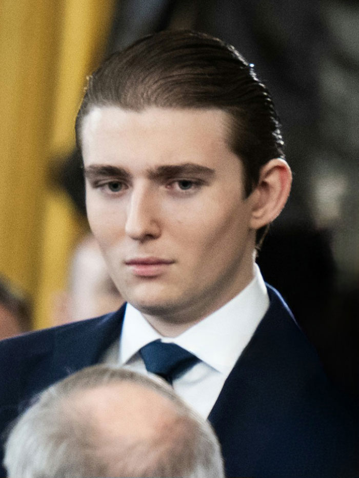Barron Trump in a formal suit, appearing serious during an event related to an emergency call incident.