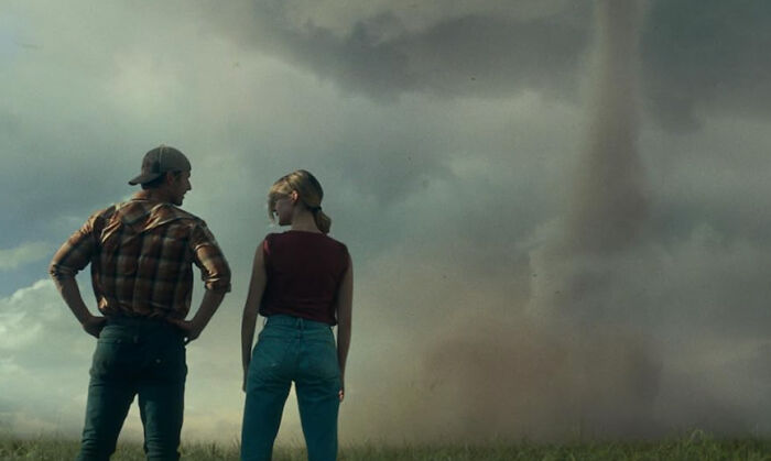 Two people standing in a field looking at a large tornado swirling in the distance, showing accidental panic.