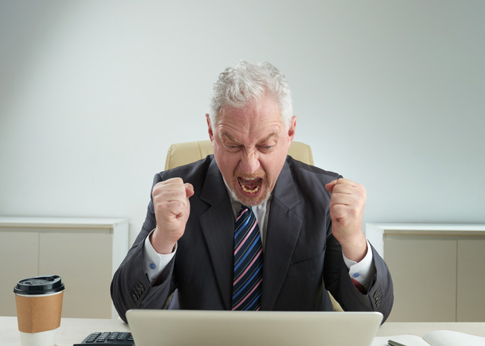 Angry American boss in suit yelling at laptop, reacting to Dutch worker logging off at 5PM and giving a reality check.