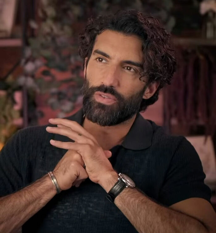 Man with dark curly hair and beard wearing black shirt and watch, speaking thoughtfully about leaked audio involving Blake Lively.