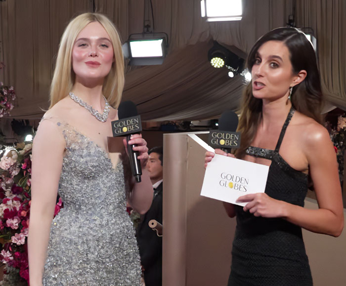 Elle Fanning standing tall in a silver gown, interviewing at the Golden Globes, showcasing women getting bigger in height.