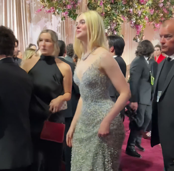 Elle Fanning standing tall at a crowded event, her height towering over other stars in a sparkling gown.