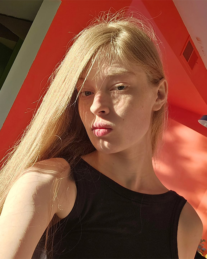 Young woman in natural light posing indoors with orange wall, related to Elon Musk making dramatic announcement about 13th child.