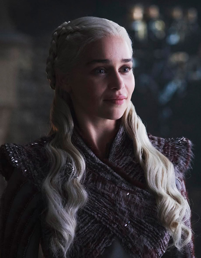 Emilia Clarke in costume on set, revealing she broke a rib during an intense intimate scene with three men.