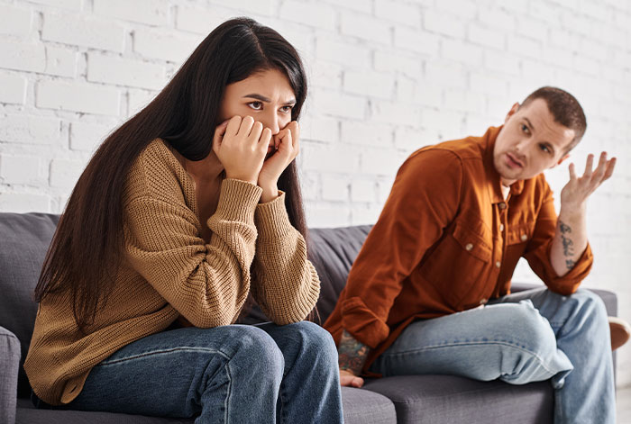 Woman upset on couch threatening to take ex’s dog to shelter while ex looks on, not intervening in the argument. Woman upset on couch threatening to take ex’s dog to shelter while ex looks on, not intervening in the argument.